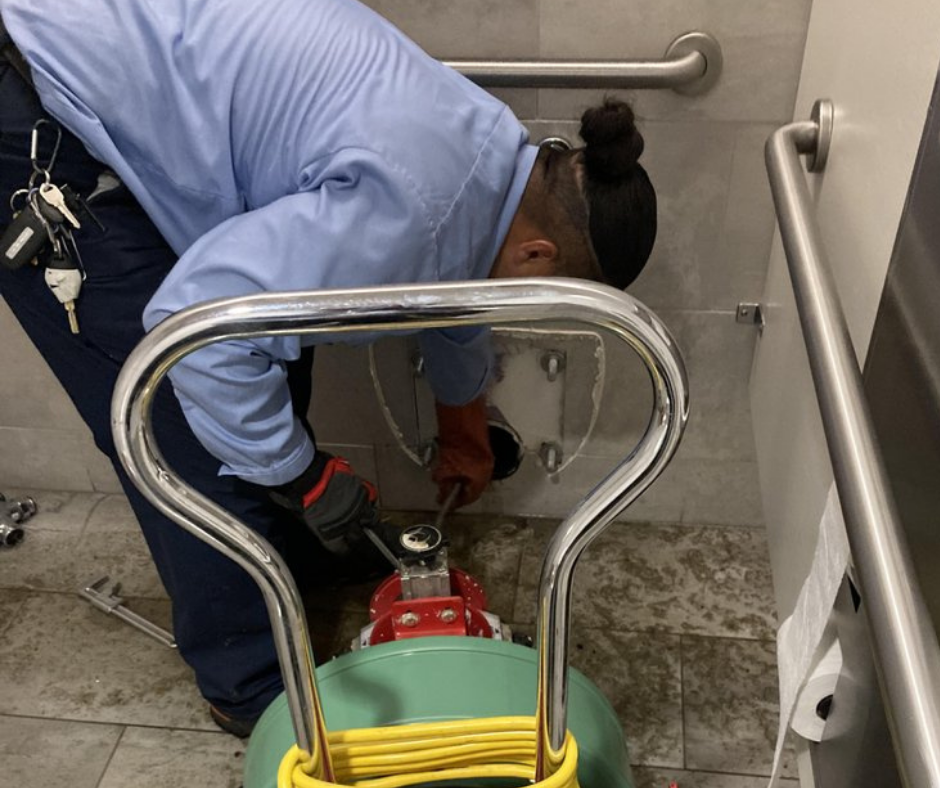Plumber clearing a commercial restroom drain with drain cleaning equipment