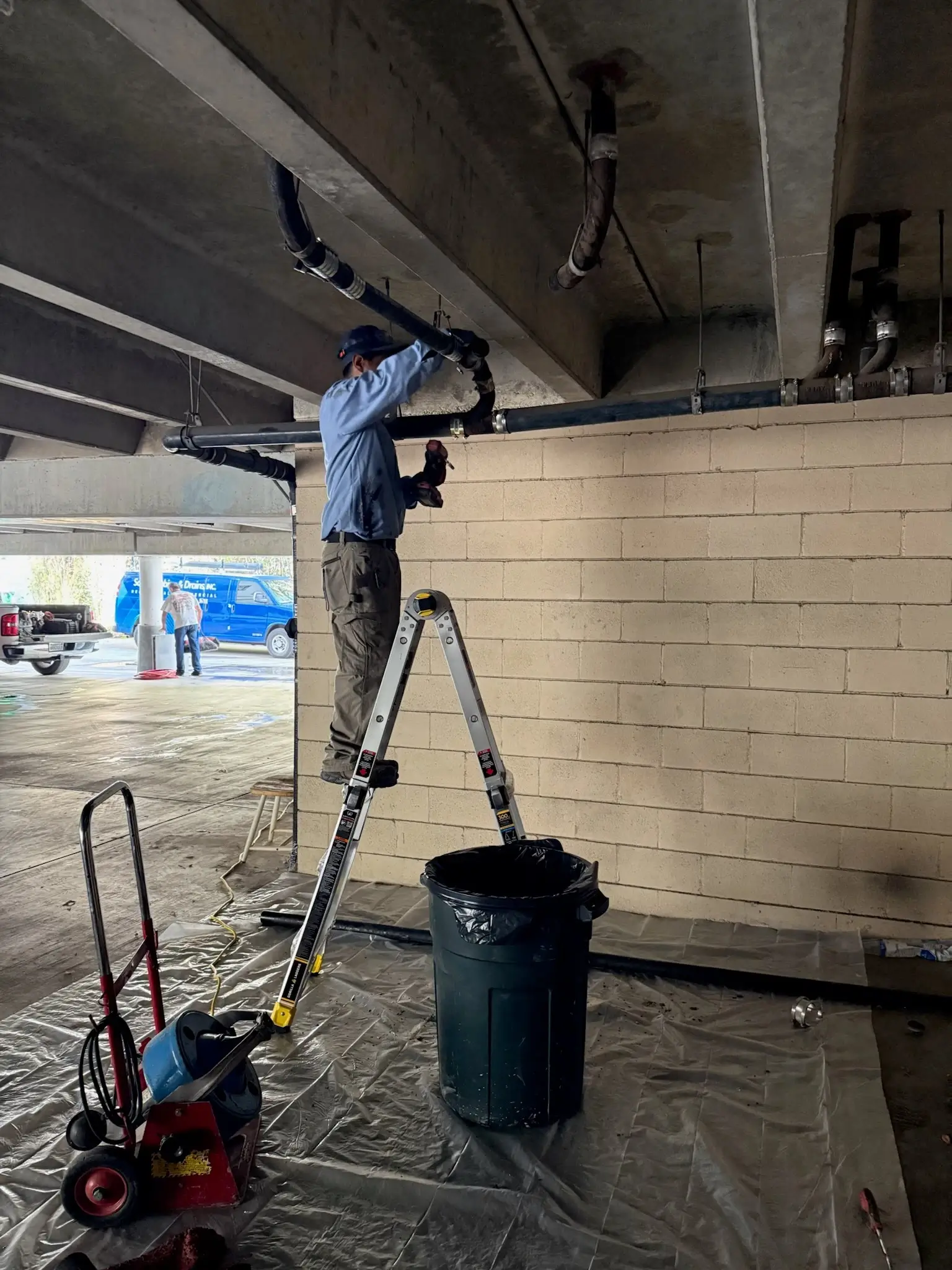 Plumber repairing commercial drain piping in a parking structure
