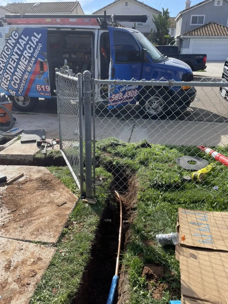 Residential driveway excavation to access underground plumbing pipes for repair or replacement.