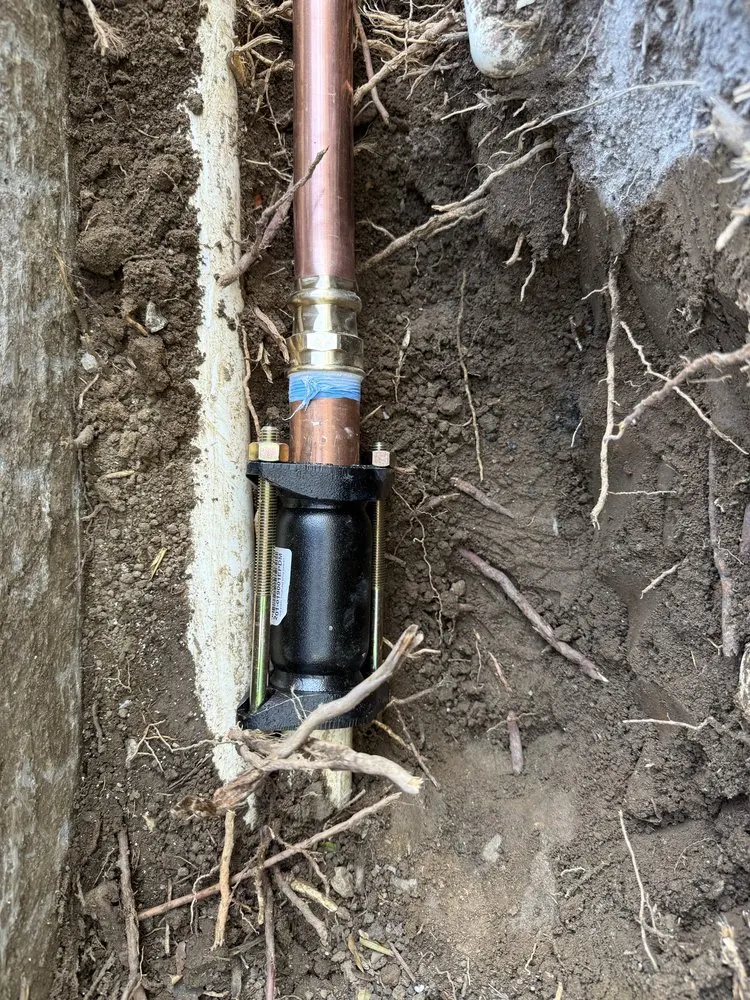 Underground copper plumbing pipe connected with metal fittings inside an excavated trench.